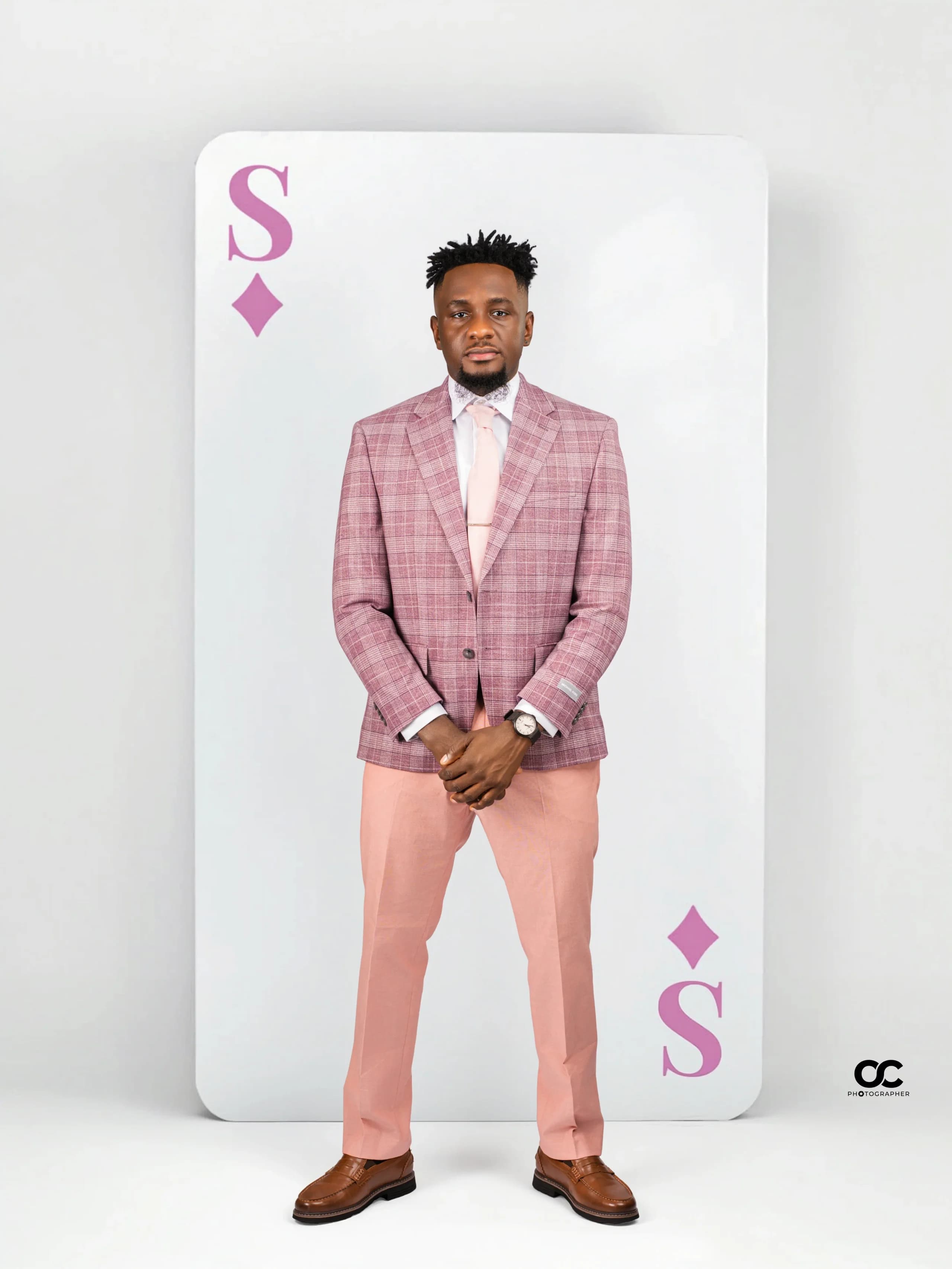 Man in a pink plaid suit with hands clasped, playing-card backdrop