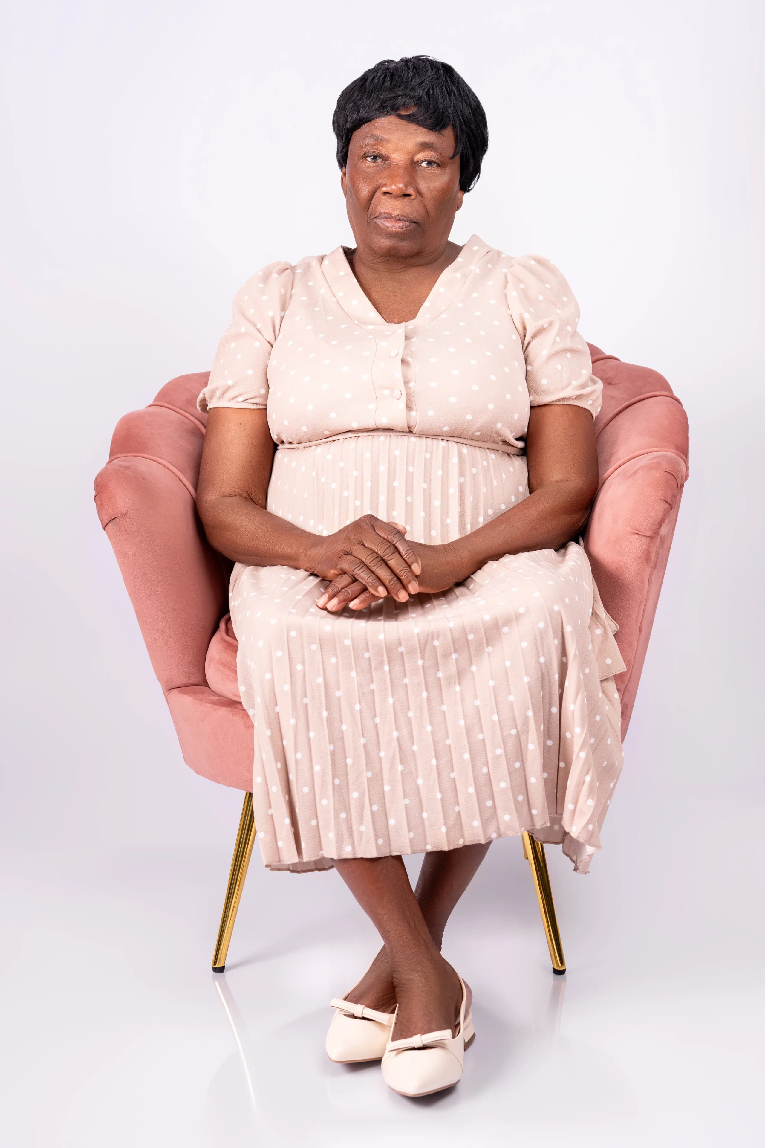 Older woman in a polka-dot dress seated in a pink armchair