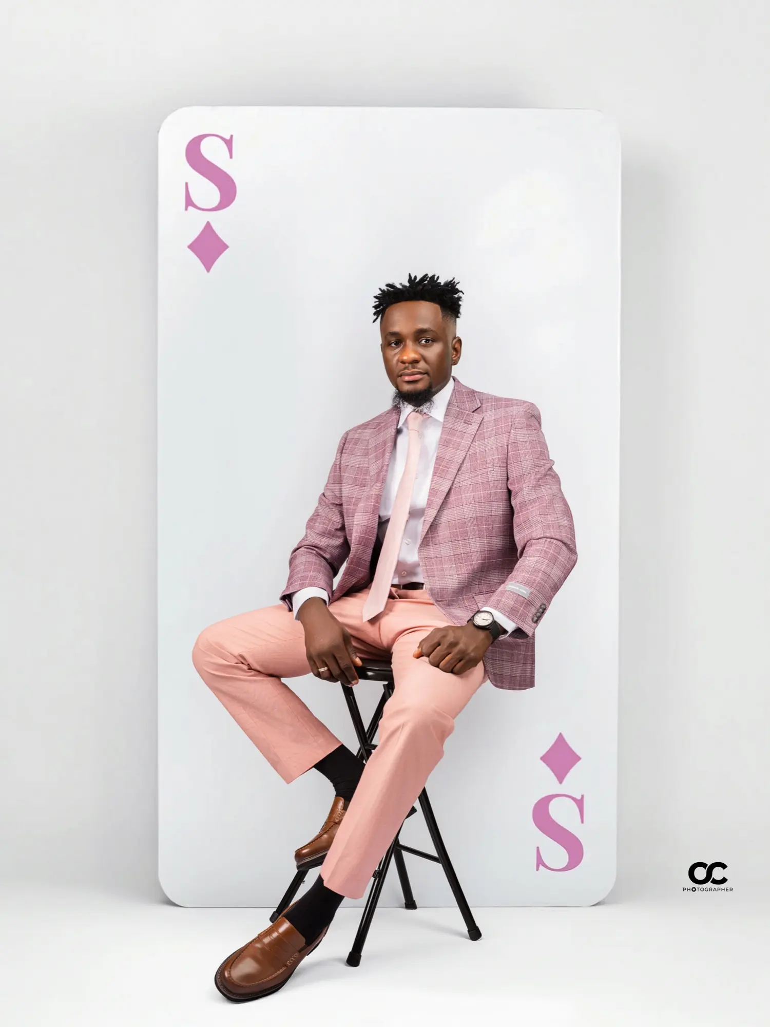 Man in a pink plaid suit seated in front of a giant playing-card backdrop