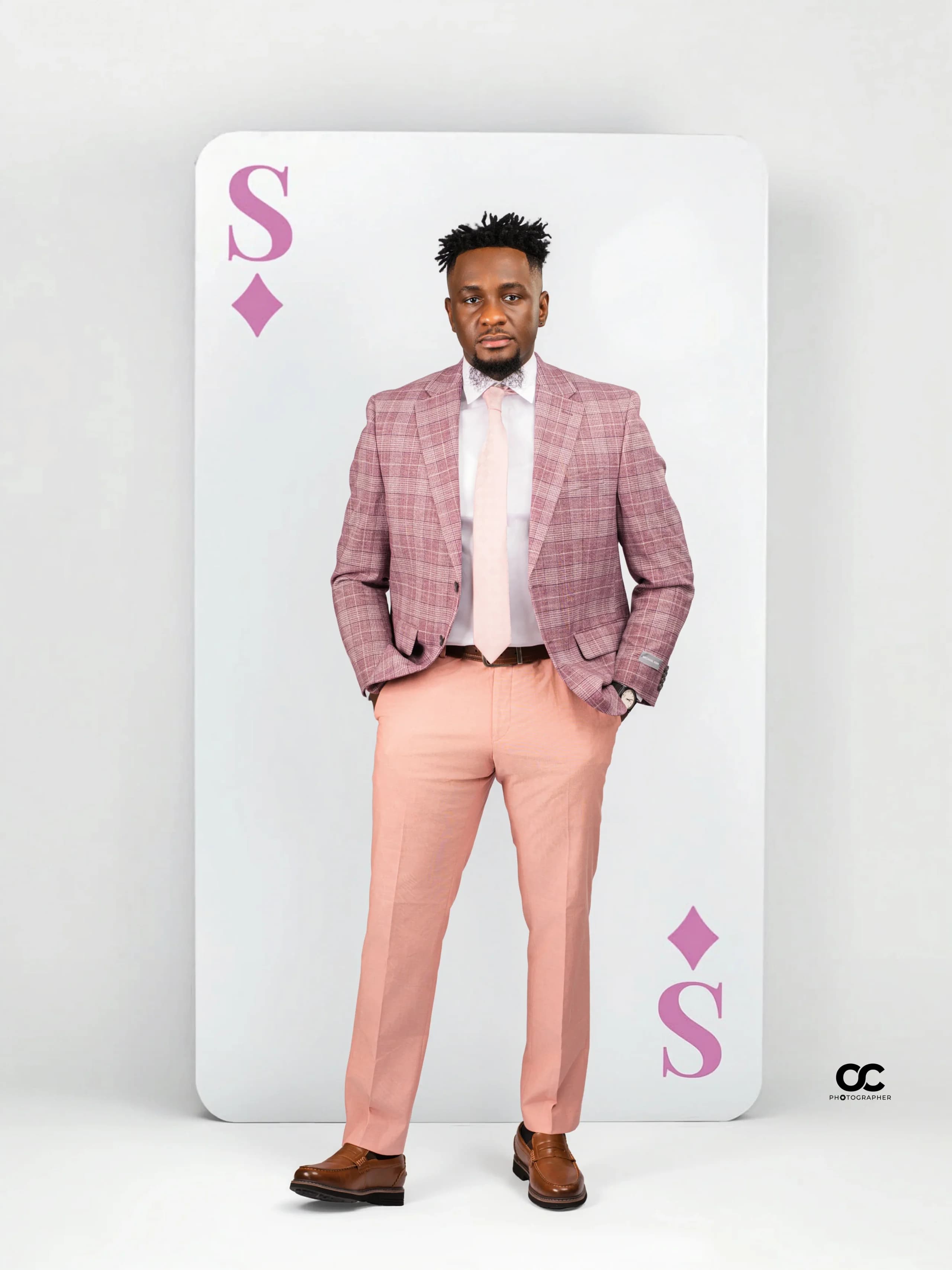 Man in a pink plaid suit standing before a giant playing-card backdrop